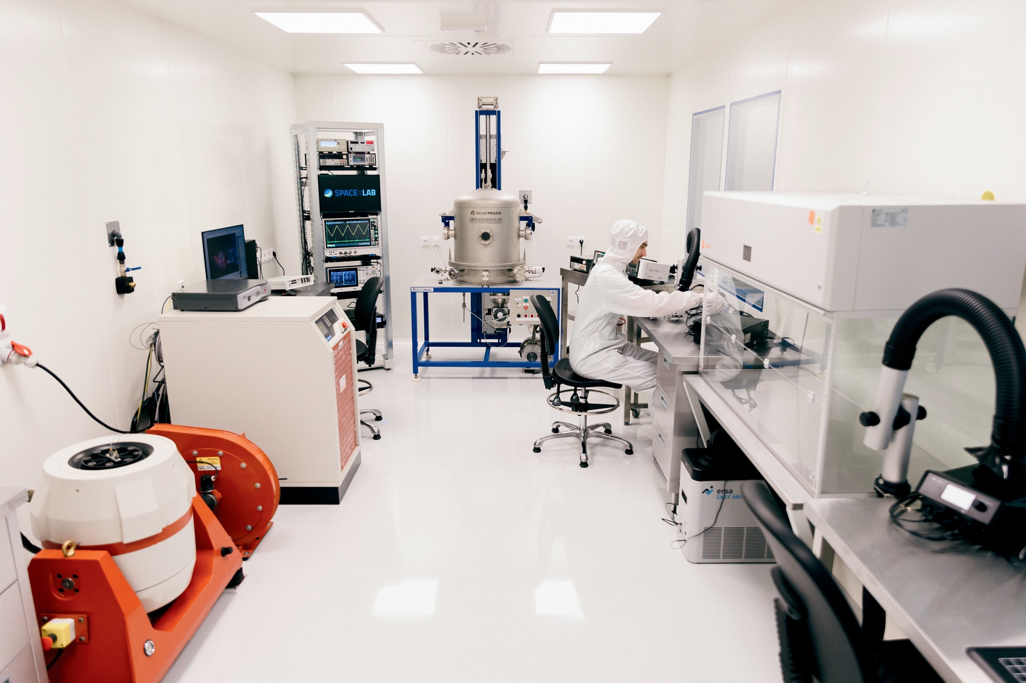 A person in white cleanroom garb working at a laminar flow bench inside the cleanroom.