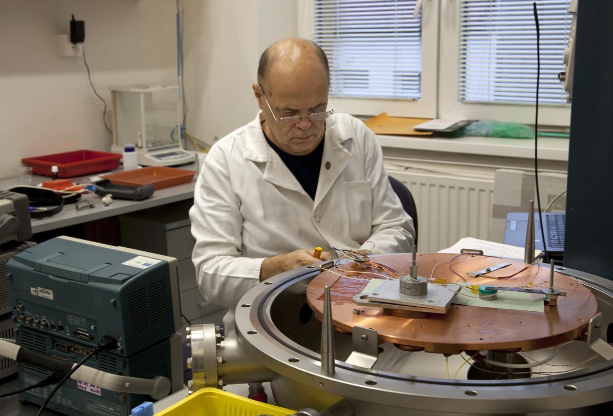 Ján Baláž wiring an instrument on the open copper baseplate of a thermal-vacuum chamber in a laboratory.