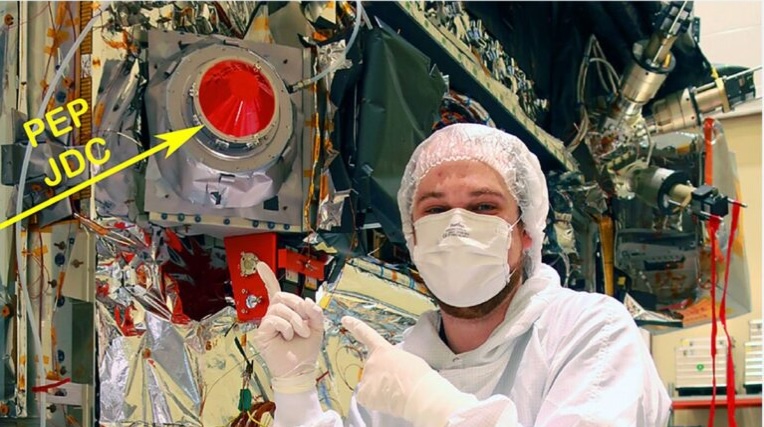 A technician in cleanroom clothing points to the PEP/JDC sensor with its red aperture cover, mounted on the JUICE spacecraft.