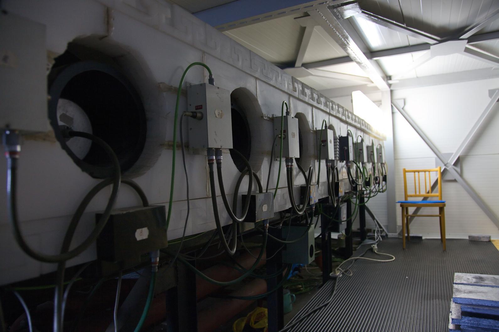 The interior of a small building containing a long neutron monitor: a row of cylindrical counter tube ends with cabling and junction boxes.