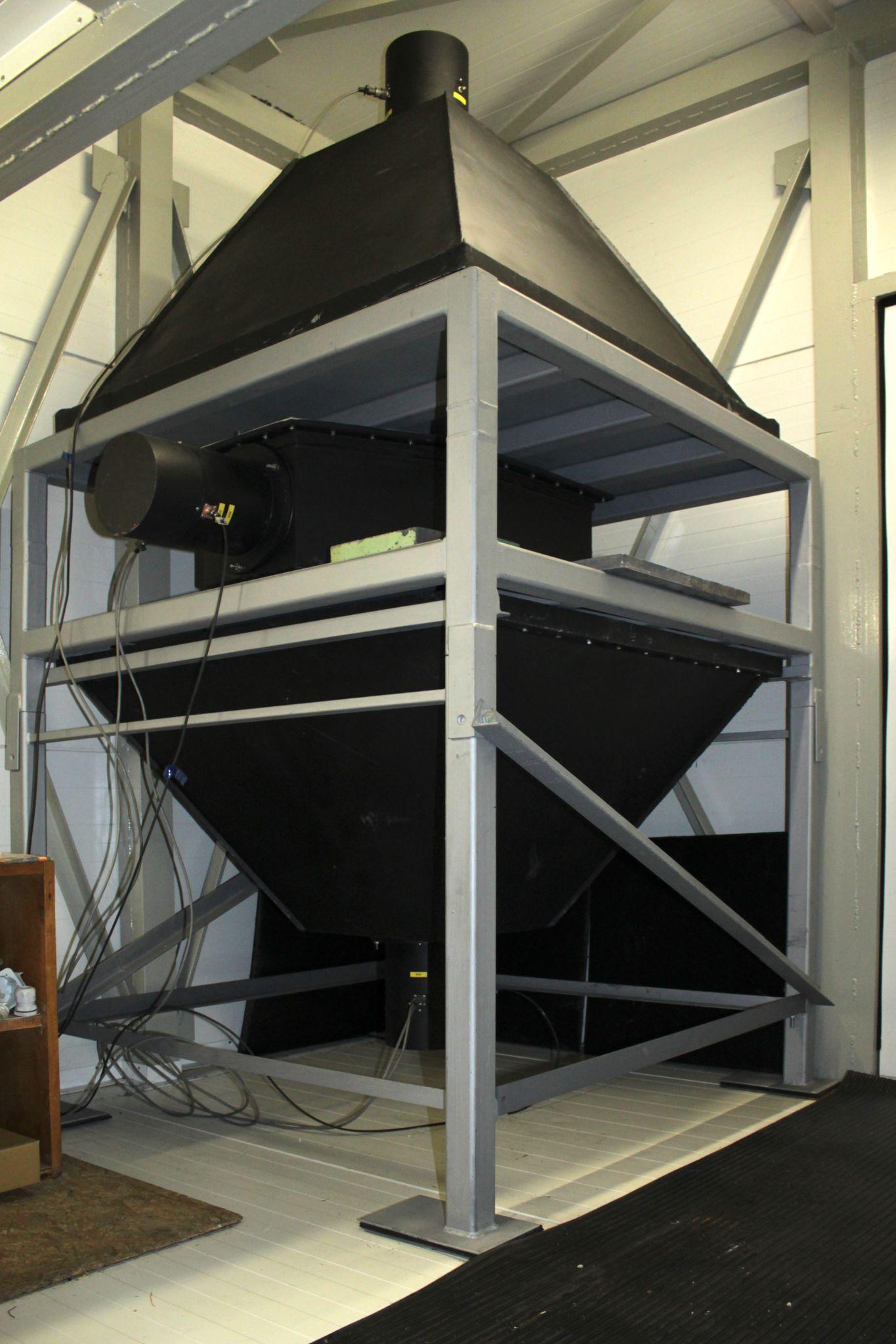 A black pyramid-shaped particle detector mounted in a steel frame inside a laboratory room.